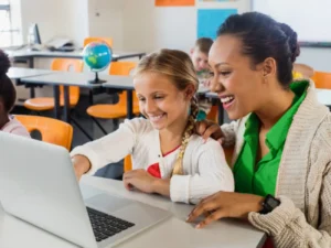 Enseignante guidant une élève avec Gingo AI sur ordinateur en classe moderne